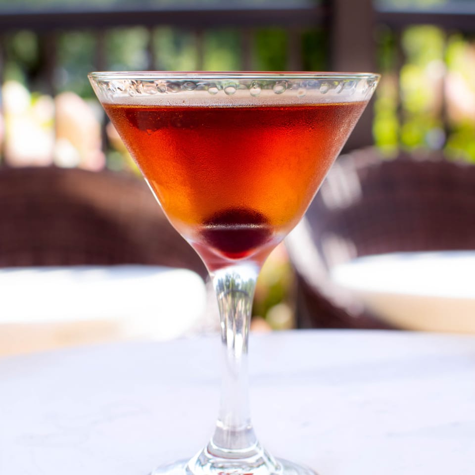 A PINO Italian restaurant cocktail, a Manhattan, with a cherry, on a white table.