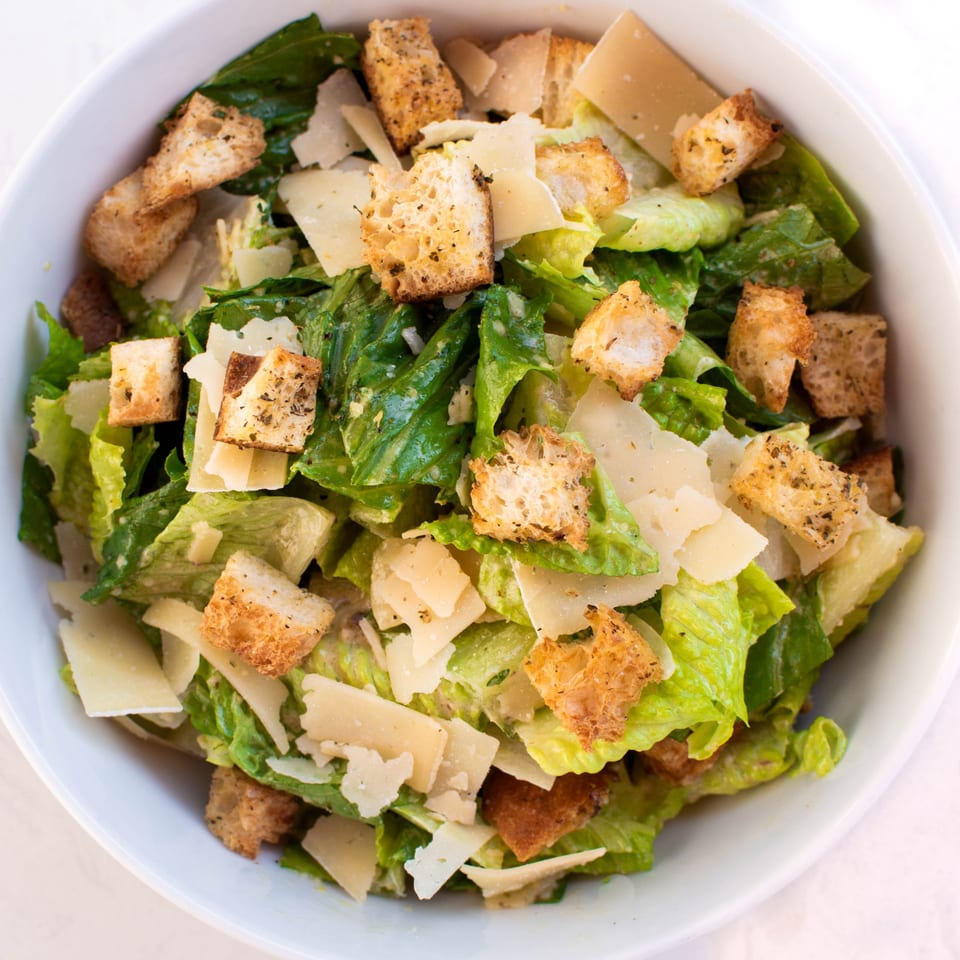 A close-up of a fresh Caesar salad with crisp romaine, parmesan shavings, and golden croutons.