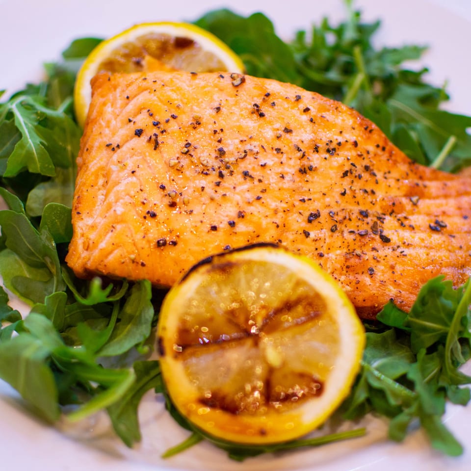 Grilled salmon fillet with cracked pepper, served on a bed of fresh arugula with lemon slices.