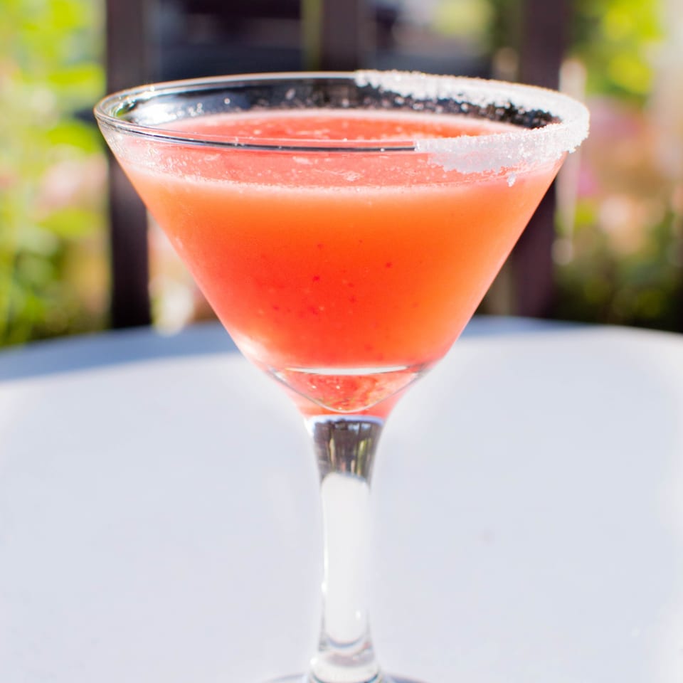 A vibrant red martini with a sugared rim sits on a white table outdoors at PINO.