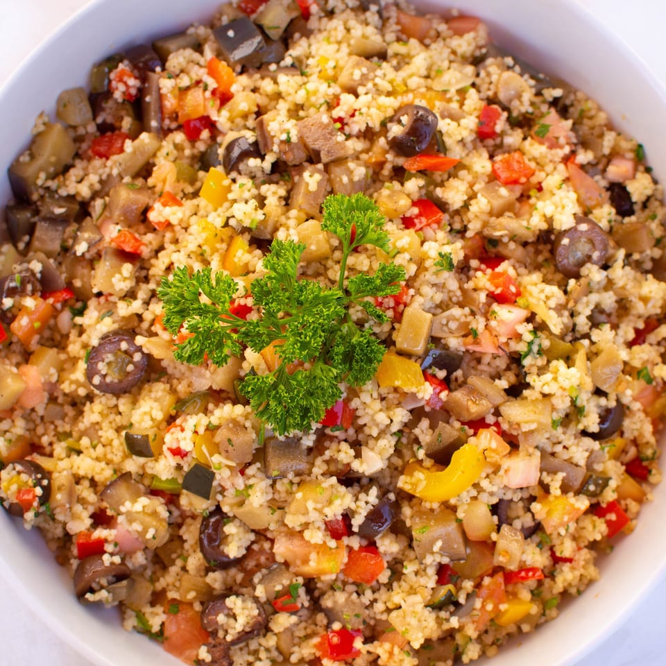 Close-up of a vibrant couscous salad with diced vegetables and fresh parsley in a white bowl.