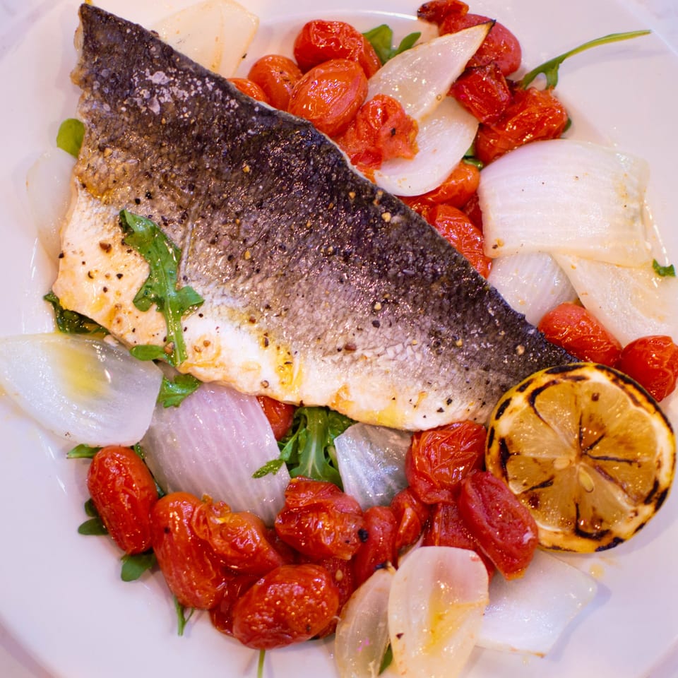 Pino's Italian sea bass with crispy skin, roasted cherry tomatoes, onions, arugula, and grilled lemon.