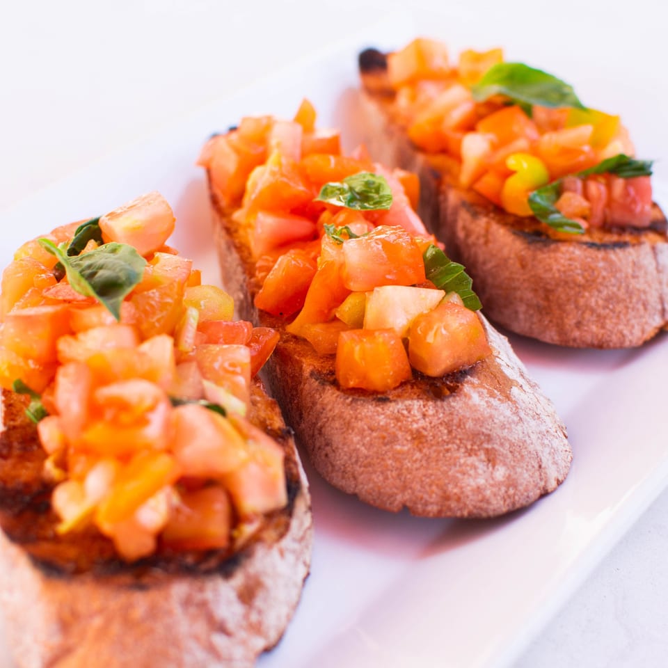 Three pieces of PINO's Italian bruschetta, topped with diced tomatoes and fresh basil, on a white plate.