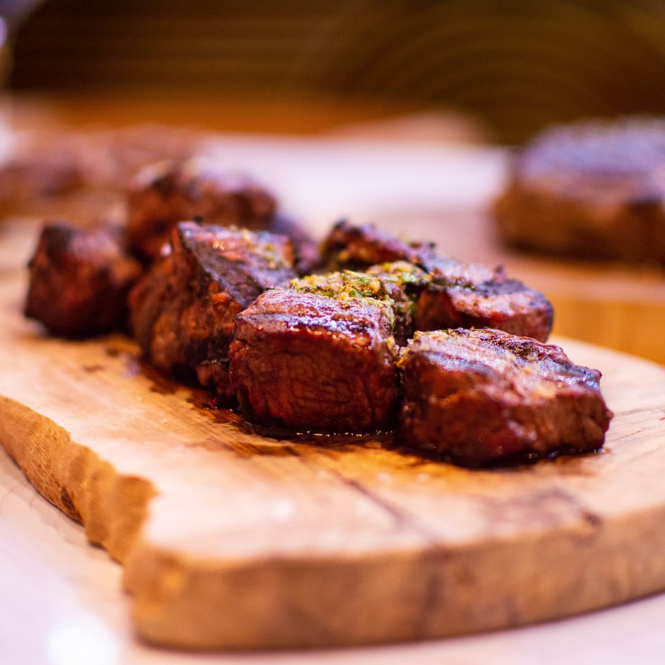 Close-up of several grilled steak pieces with herbs on a rustic wooden board at PINO.