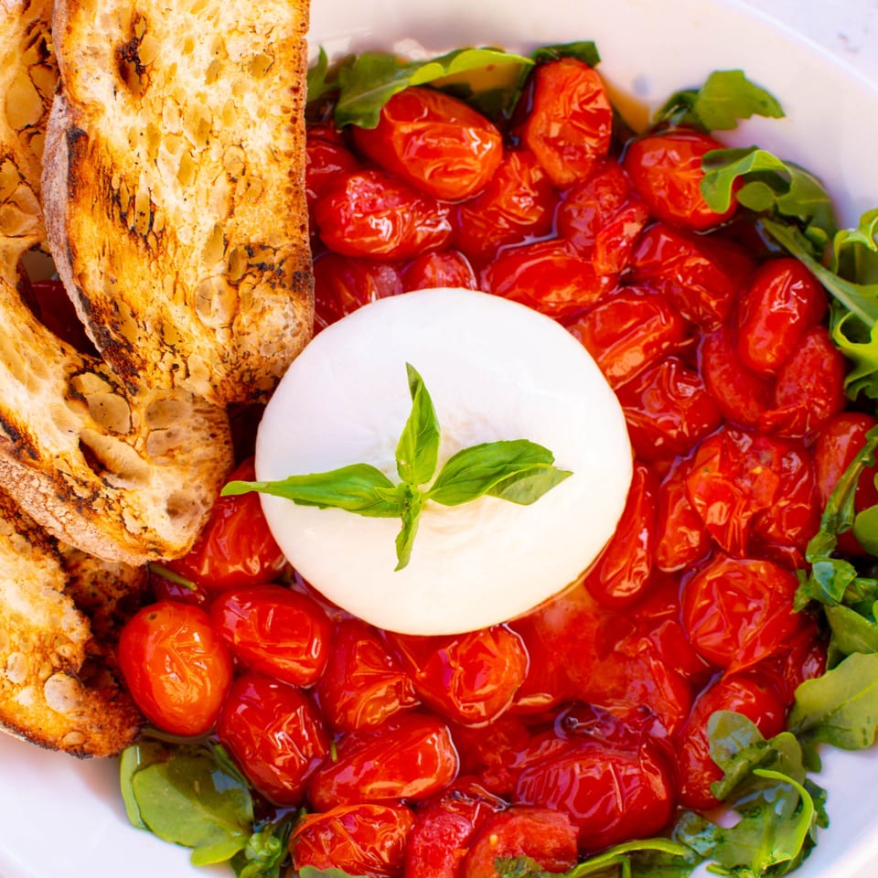 Burrata cheese with roasted cherry tomatoes, fresh basil, arugula, and toasted bread at PINO.